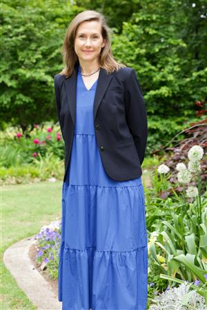 Beth Gulewich wearing a blazer and a blue dress standing in a garden